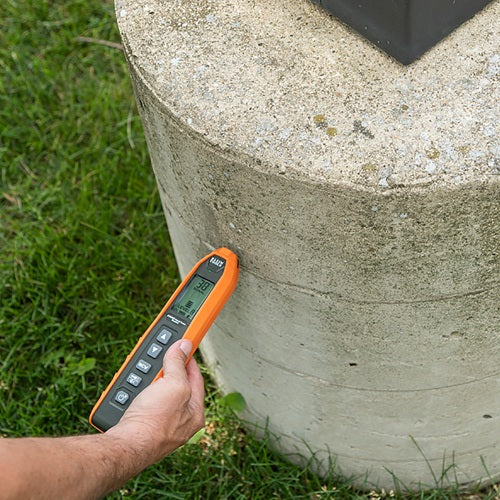 Person using a digital thermometer on a concrete surface outdoors