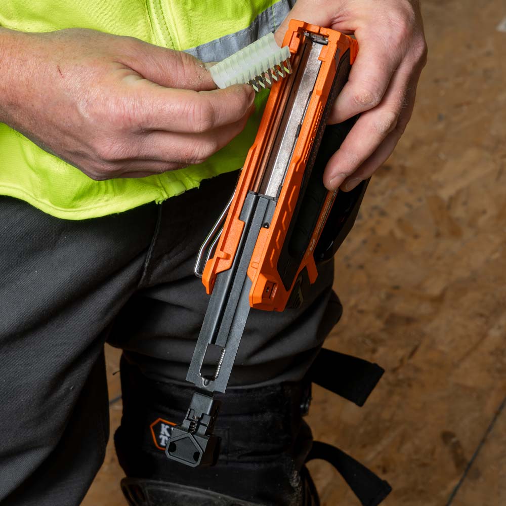 Person holding a tool with an orange handle and black blade, wearing a high-visibility jacket.
