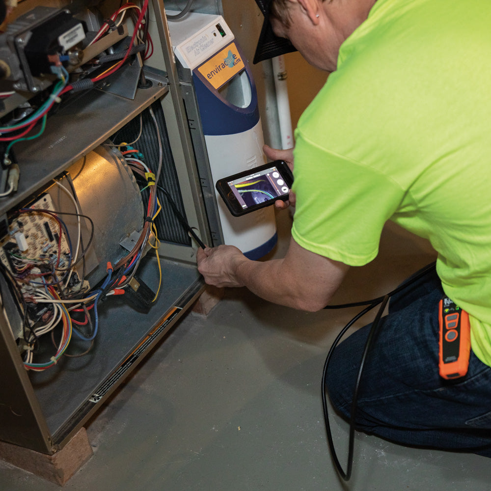 Person working on an electrical panel with a device and smartphone.