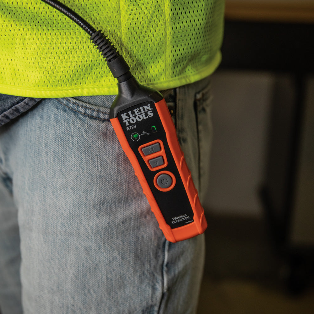 Orange and black Klein Tools device on a person wearing a yellow safety vest and blue jeans.