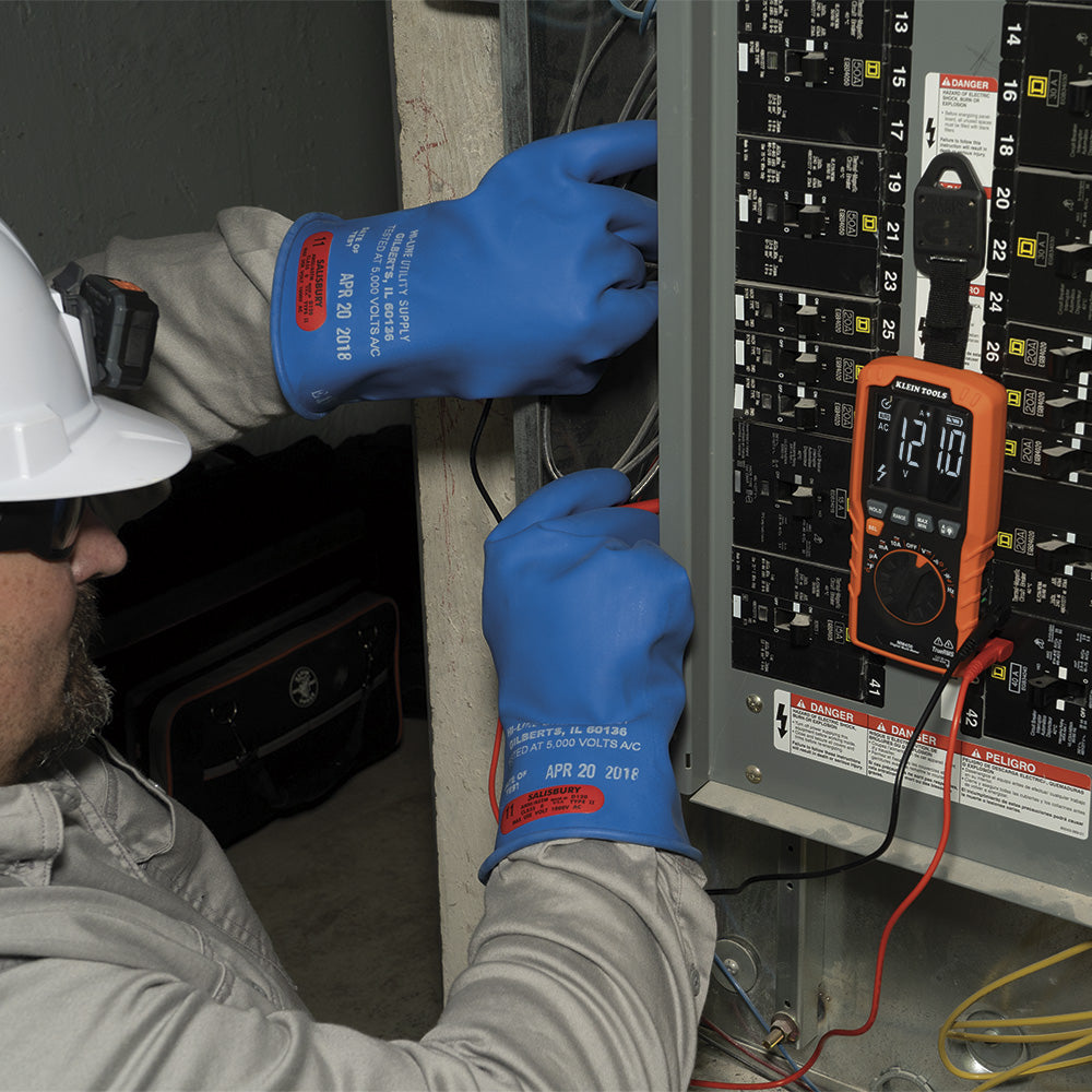Person wearing blue gloves and a hard hat working on an electrical panel with a multimeter.