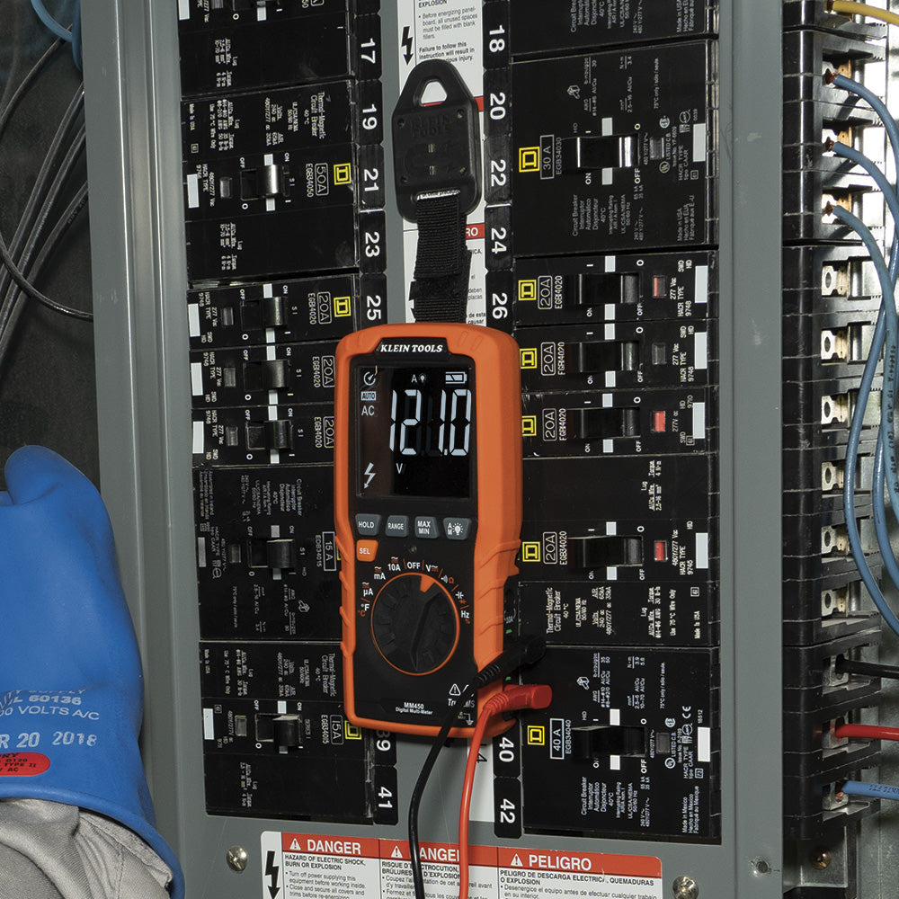 Multimeter on a panel with numbered circuits and a blue glove partially visible