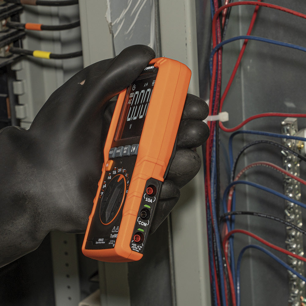 Hand wearing a black glove holding an orange multimeter against electrical panels and wires.