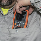 Person holding an orange multimeter close to their face, wearing a gray jacket.