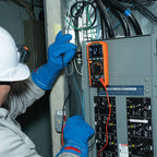 Person wearing a hard hat and blue gloves using a multimeter on electrical equipment.