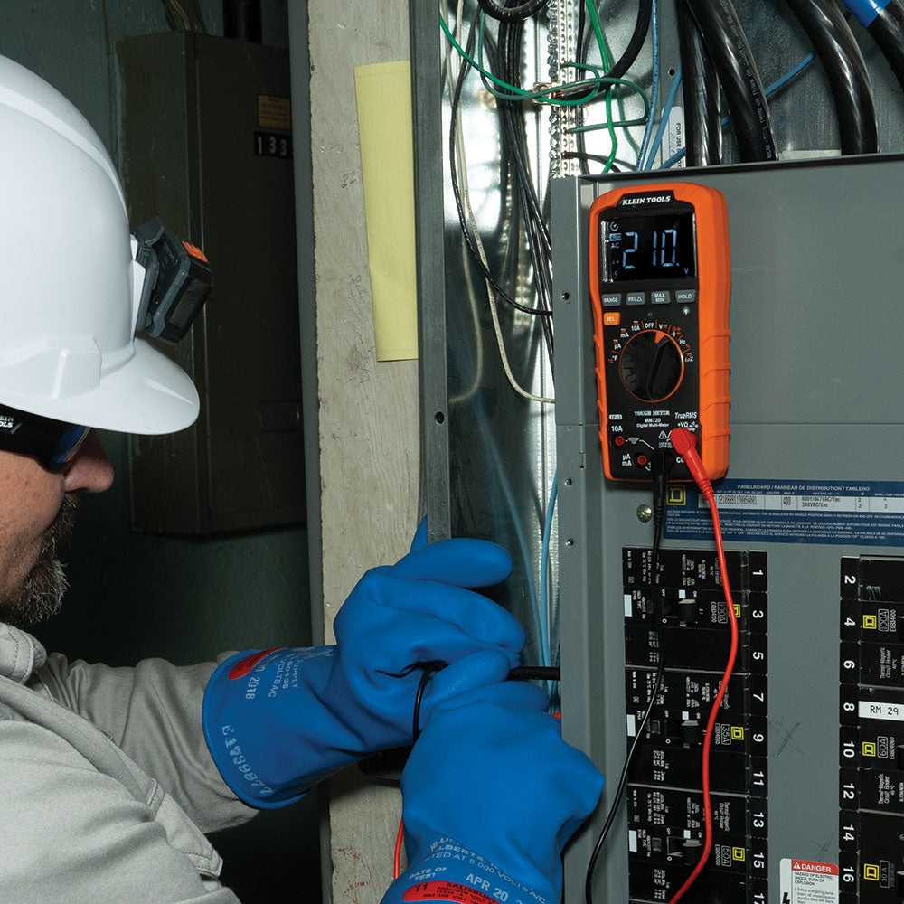 Person wearing a hard hat and blue gloves using an orange multimeter on electrical panels.