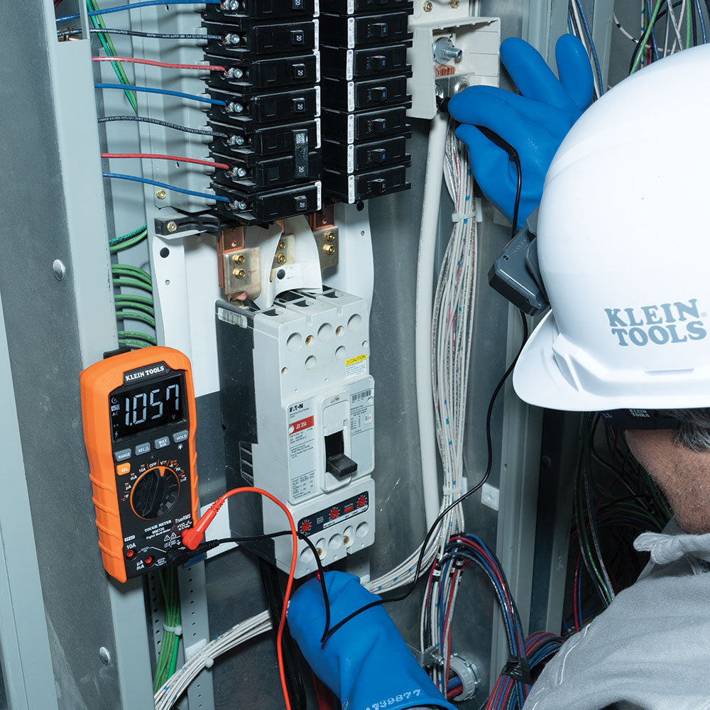 Person wearing a hard hat and gloves working on electrical panel with multimeter