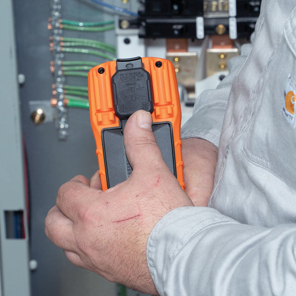 Person holding an orange and black device in front of a control panel.