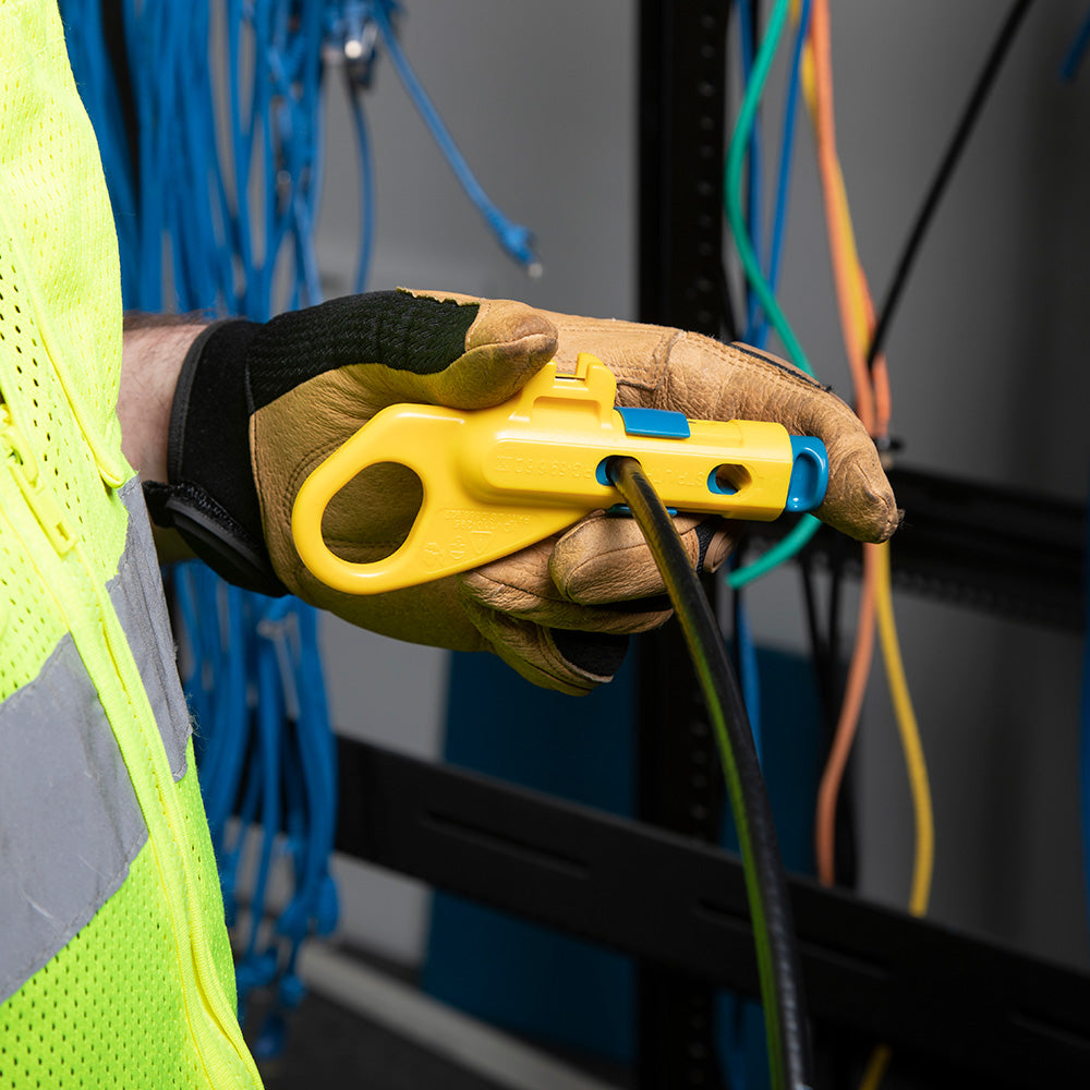 Hand wearing a brown glove holding a yellow tool with wires in the background