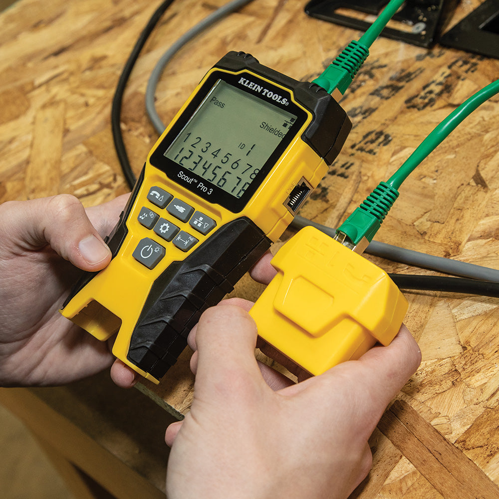 Person holding a yellow Klein Tools multimeter on a wooden surface