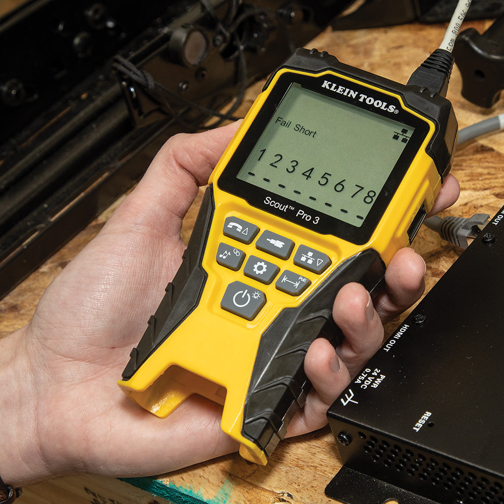 Hand holding a yellow and black Klein Tools device on a wooden surface