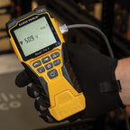 Yellow Klein Tools multimeter held by a gloved hand with a blurred background