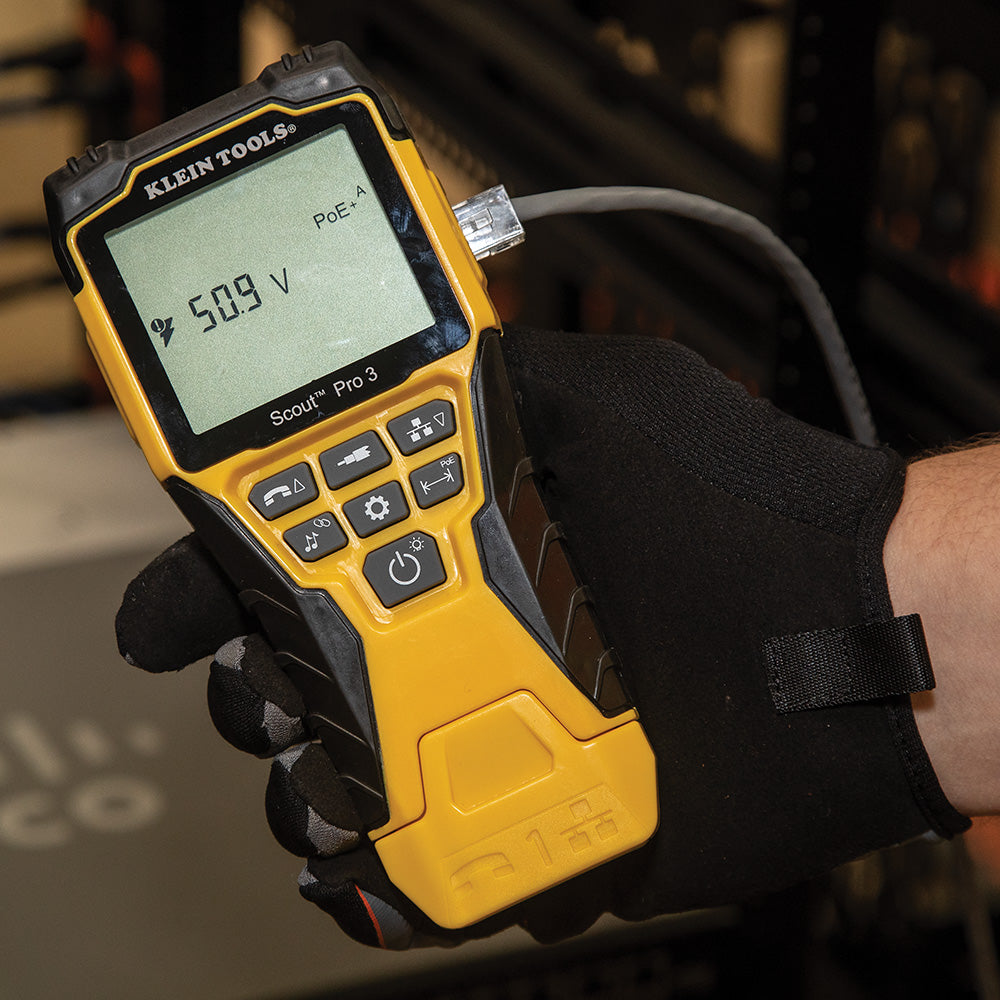 Yellow Klein Tools multimeter held by a gloved hand with a blurred background