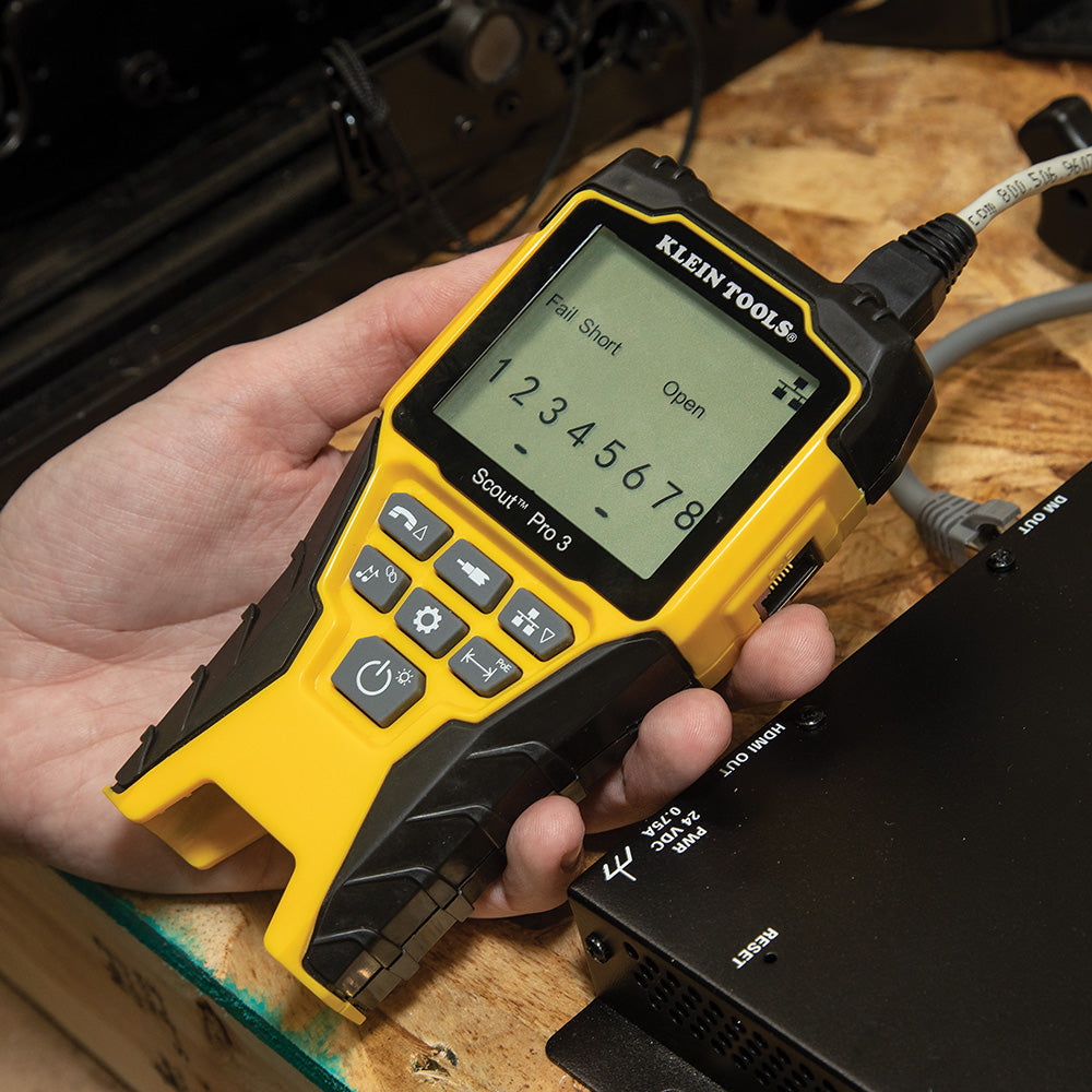 Hand holding a yellow Klein Tools multimeter on a wooden surface