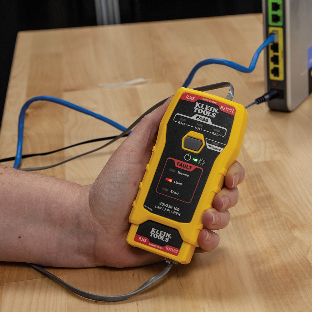Hand holding a yellow Klein Tools network cable tester on a wooden surface