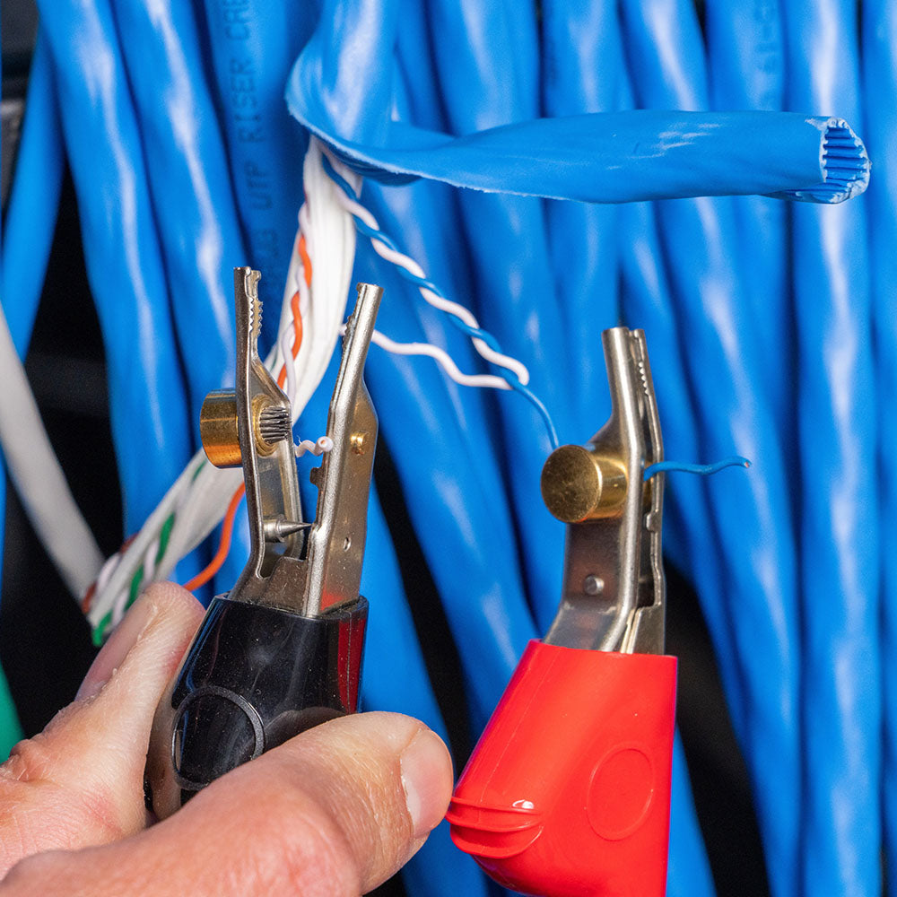Person working with pliers on a blue Ethernet cable against a blue curtain background